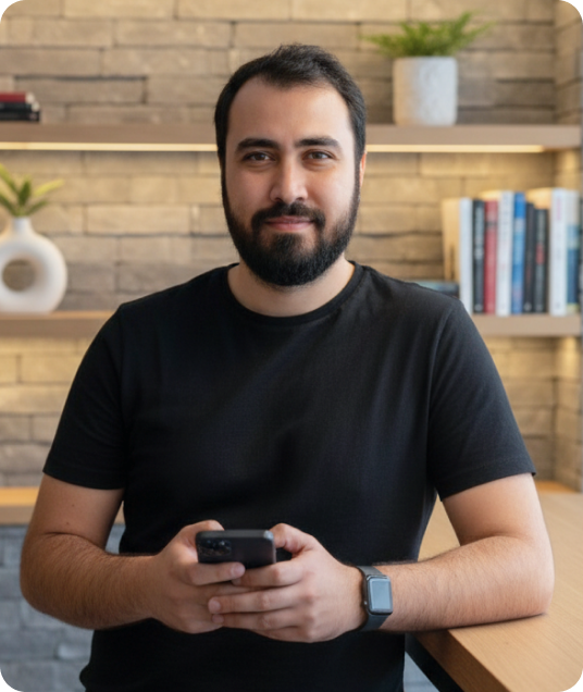 Foto do Bruno Silva, homem com barba e cabelo escuro olhando para o lado, vestindo uma jaqueta preta, em frente à Tower Bridge, em Londres, em um dia nublado.